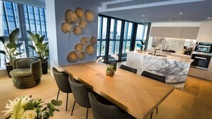 A modern kitchen with a marble countertop, a dining area with a wooden table and chairs, and a large window providing a view of the city.