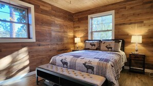 A wooden cabin bedroom with a bed, two bedside lamps, a bench, and a ceiling fan. - Lone Star Lodge in Whispering Pines w/ Mountain View - Epic Pickleball Fun!
 (Payson)