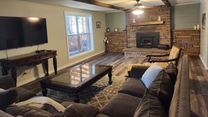 A living room with a stone fireplace, a large window, a flat-screen TV, and a cozy seating area. - Lone Star Lodge in Whispering Pines w/ Mountain View - Epic Pickleball Fun!
 (Payson)