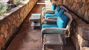 A covered patio area with wicker furniture and stone walls. - Lone Star Lodge in Whispering Pines w/ Mountain View - Epic Pickleball Fun!
 (Payson)