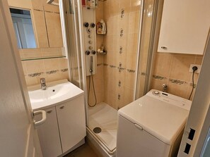 A compact bathroom with a sink, a shower enclosure, and a washing machine.
