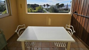 A balcony with a white table and chairs, a view of a garden, and a wooden fence.