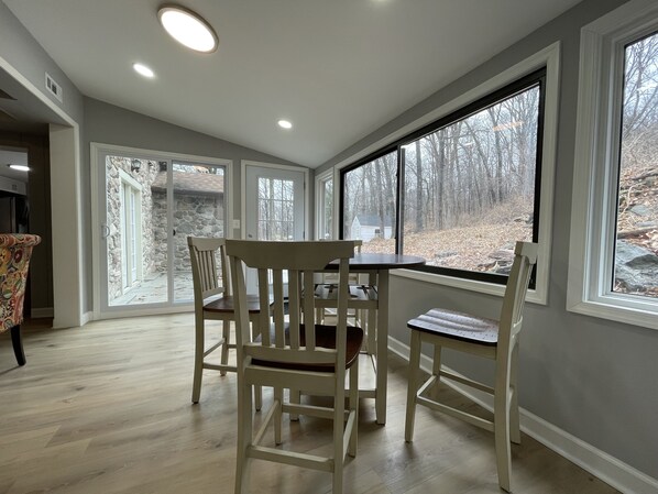 A dining area with a stone exterior wall, large windows, and a view of a wooded area.