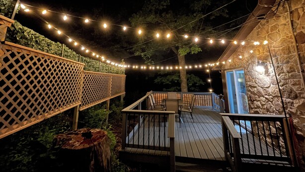 A wooden deck with string lights, a stone wall, and a wooden fence. - Entire Mountain Cottage Near Scenic Hiking Trails, Your Getaway Retreat! (Smithsburg)