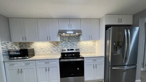 A modern kitchen with white cabinets, a stainless steel refrigerator, a microwave, and a stove. - Entire Mountain Cottage Near Scenic Hiking Trails, Your Getaway Retreat! (Smithsburg)