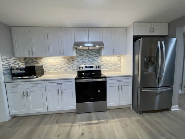Una cocina moderna con armarios blancos, un refrigerador de acero inoxidable, un microondas y una estufa.