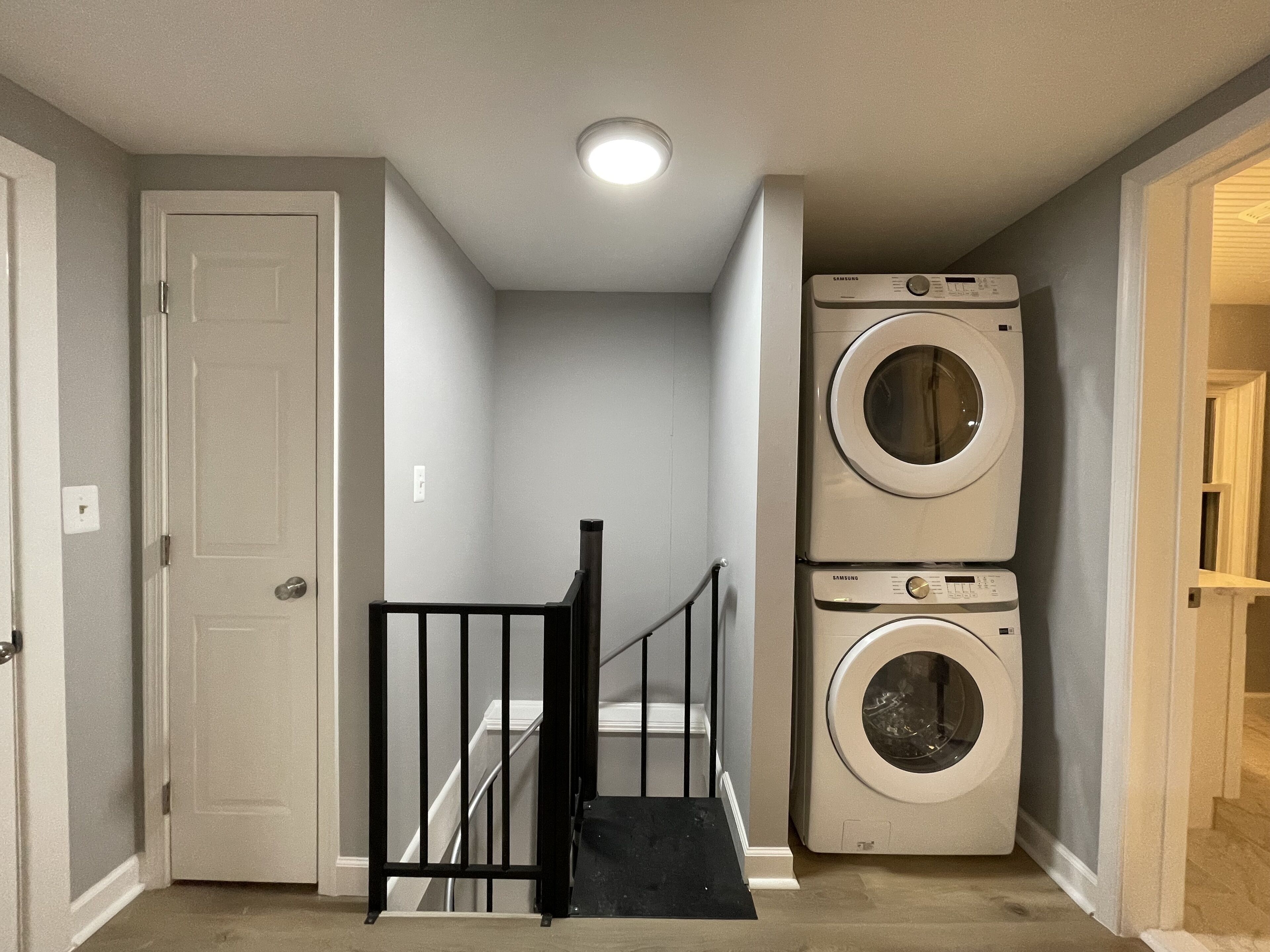 A laundry room with two stacked washers and dryers, a black railing, and a white door.