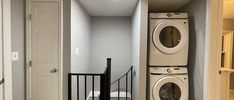 A laundry room with two stacked washers and dryers, a black railing, and a white door.