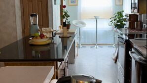 A kitchen with a central island, a dining area with a white table and chairs, and a view of the living room through a glass door. - SkyGazers Delight. One of the Safest areas in Bloomington. Super easy access!! (Bloomington)