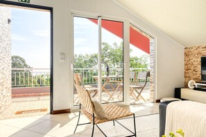 Ein Zimmer mit Balkon, einem Korbstuhl, einem Bett und einem Fernseher.