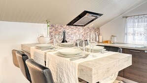 A dining area with a marble table set for four, a brick backsplash, and a modern kitchen in the background. - Cantinho da Mikaela, a Home in Madeira (Ponta do Sol)