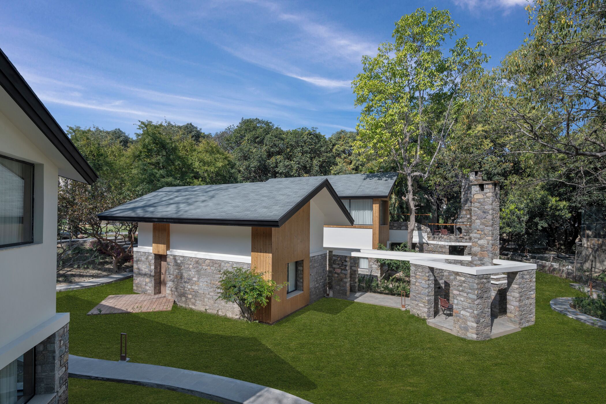 Une maison moderne avec une façade en pierre, une terrasse en bois et une pelouse bien entretenue.