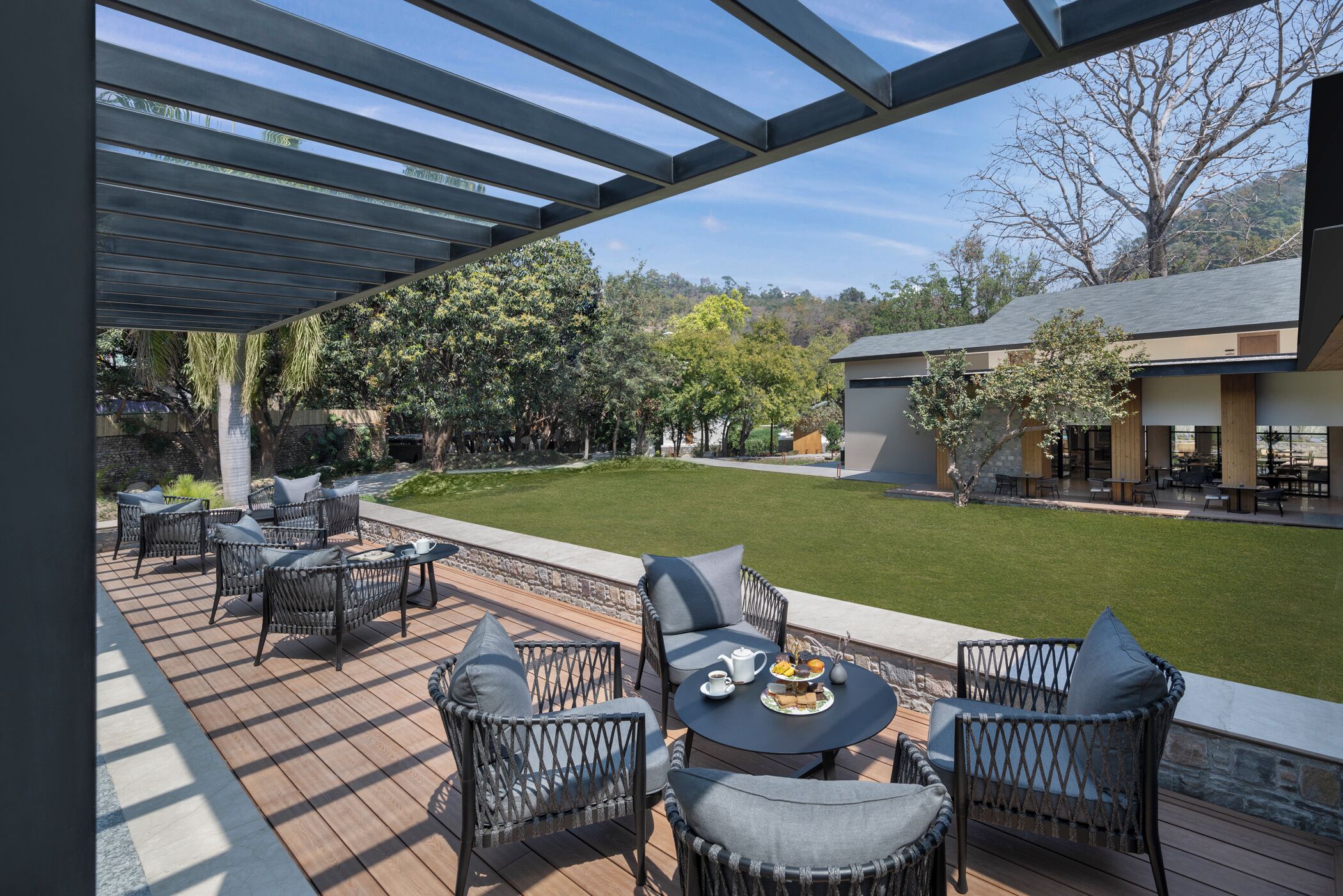 Un espace extérieur aménagé en terrasse, avec des meubles en osier et une table ronde, donnant sur une pelouse bien entretenue et un bâtiment situé au loin.