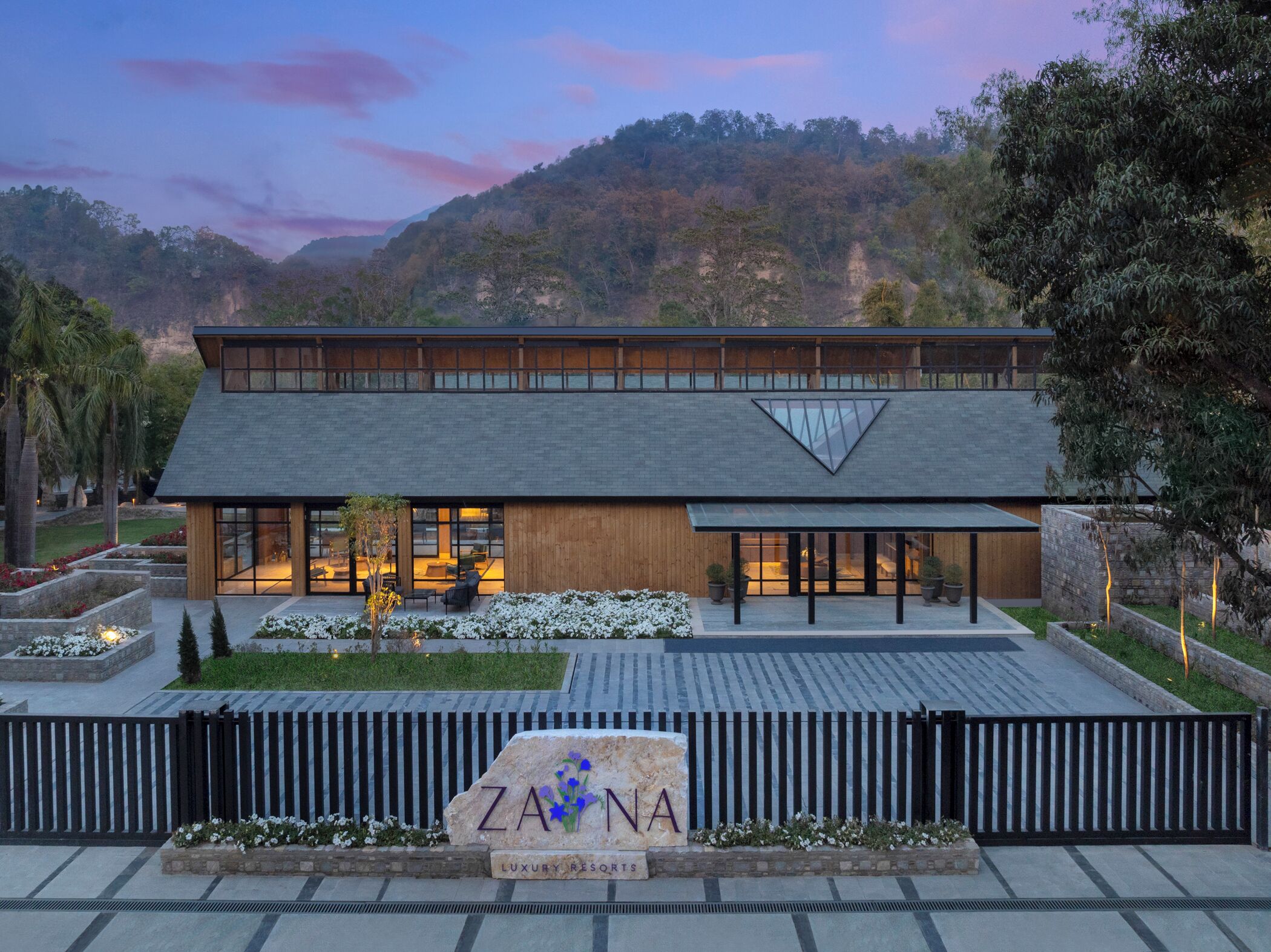 A modern two-story building with a flat roof, large windows, and a stone sign with the name "ZANNA LUXURY RESORTS".