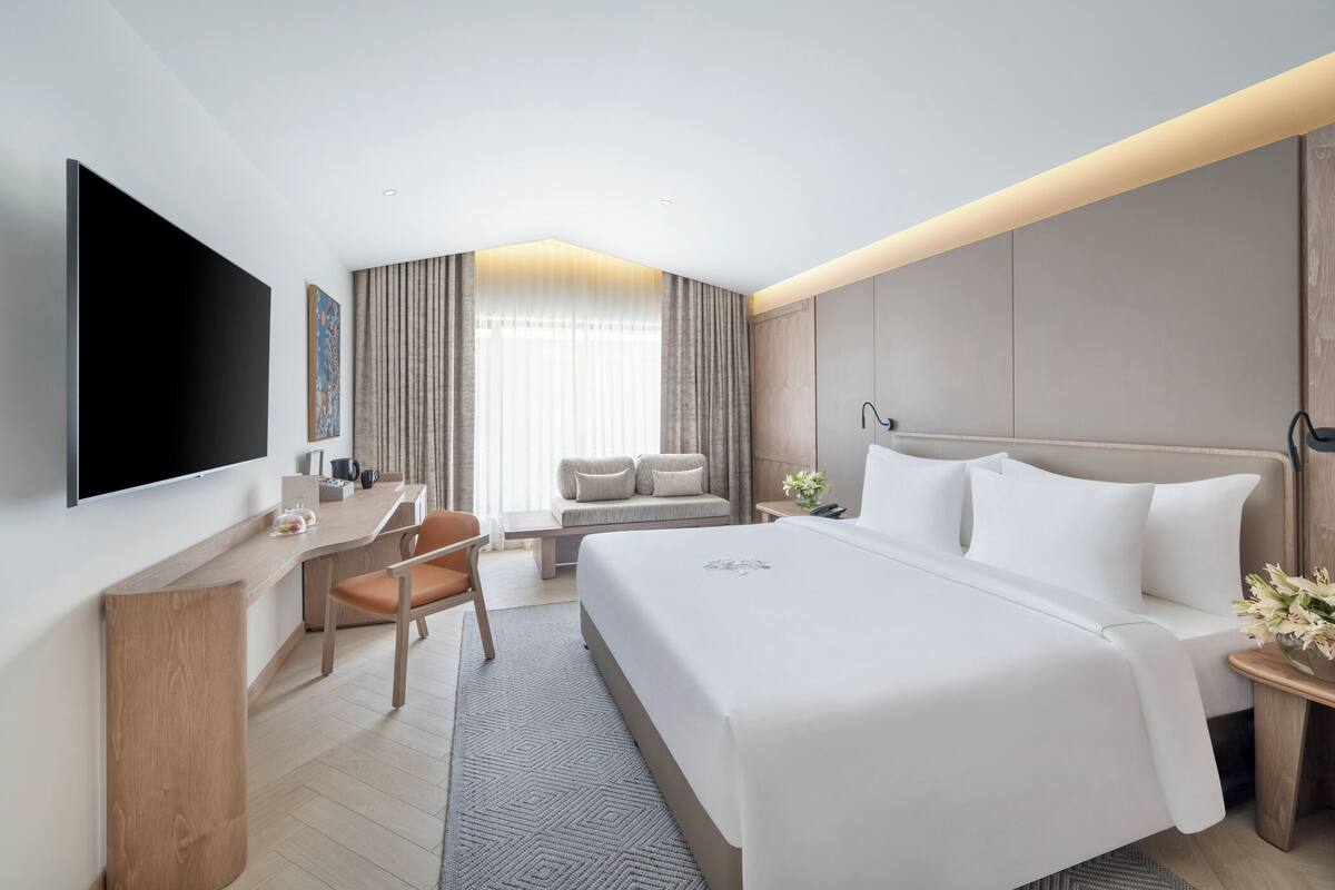 Een moderne hotelkamer met een groot bed, een bureau, een flatscreen televisie en een zithoek met uitzicht op het omliggende landschap.