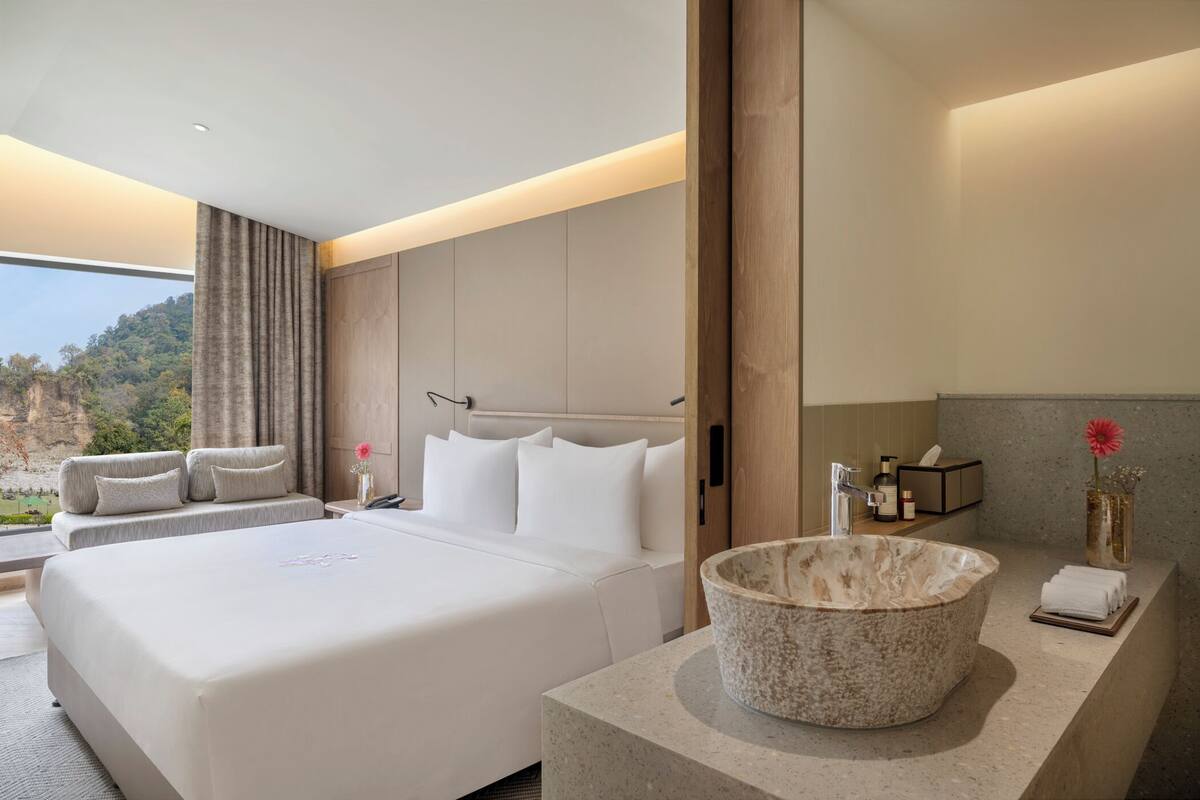 Een moderne hotelkamer met een groot bed, een stenen wastafel en uitzicht op een bergachtig landschap.