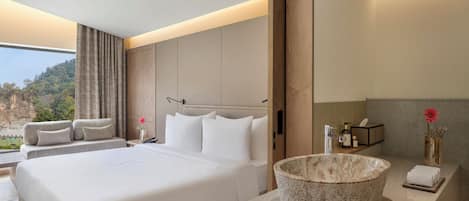 Una habitación de hotel moderna con una cama grande, un lavamanos de piedra y vistas a un paisaje montañoso.