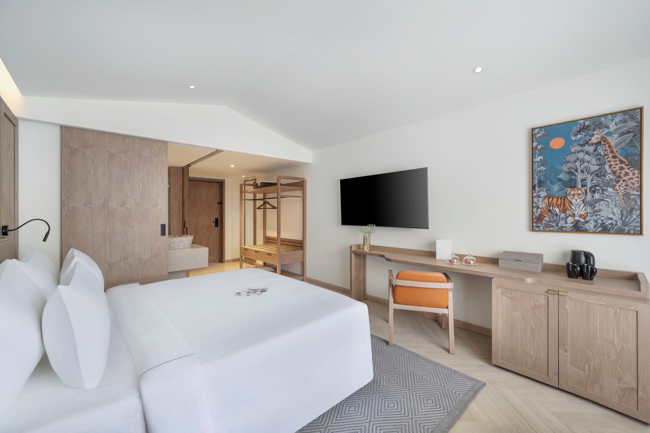 A hotel room with a bed, a desk, a chair, a TV, and a painting on the wall.