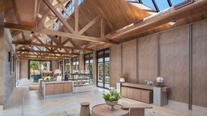 Un hall d’entrée spacieux avec des poutres en bois, un comptoir d’accueil, des coins salon et de grandes fenêtres donnant sur l’extérieur.
