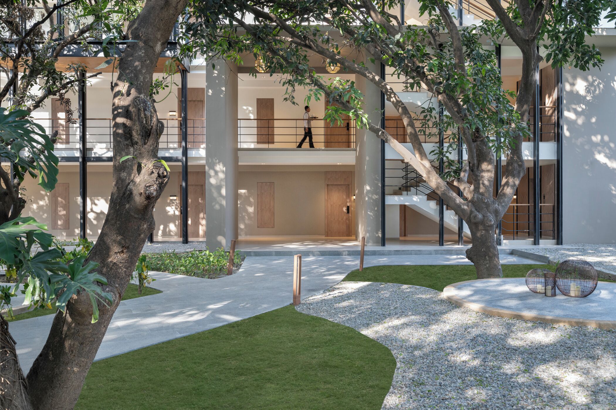 A modern building with a central courtyard, featuring a well-maintained lawn, trees, and a staircase leading to an upper level.