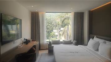 Une chambre d’hôtel moderne dotée d’un grand lit, d’un bureau avec un téléviseur à écran plat et offrant une vue sur une végétation luxuriante.