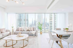 A modern living room with a sofa, coffee table, and dining table, large windows with a city view, and minimalistic decor.