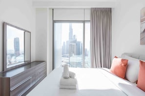 Une chambre d’hôtel dotée d’une grande fenêtre, d’un lit avec une literie blanche, d’un téléviseur à écran plat posé sur une console en bois, et offrant une vue sur le paysage urbain.