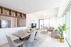 A modern living room with a sofa, a dining table with chairs, a TV, and a large window.