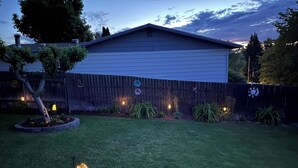 A backyard with a wooden fence, a house, and a small garden area with plants and a decorative light. - The Tangerine Door (Lewiston)
