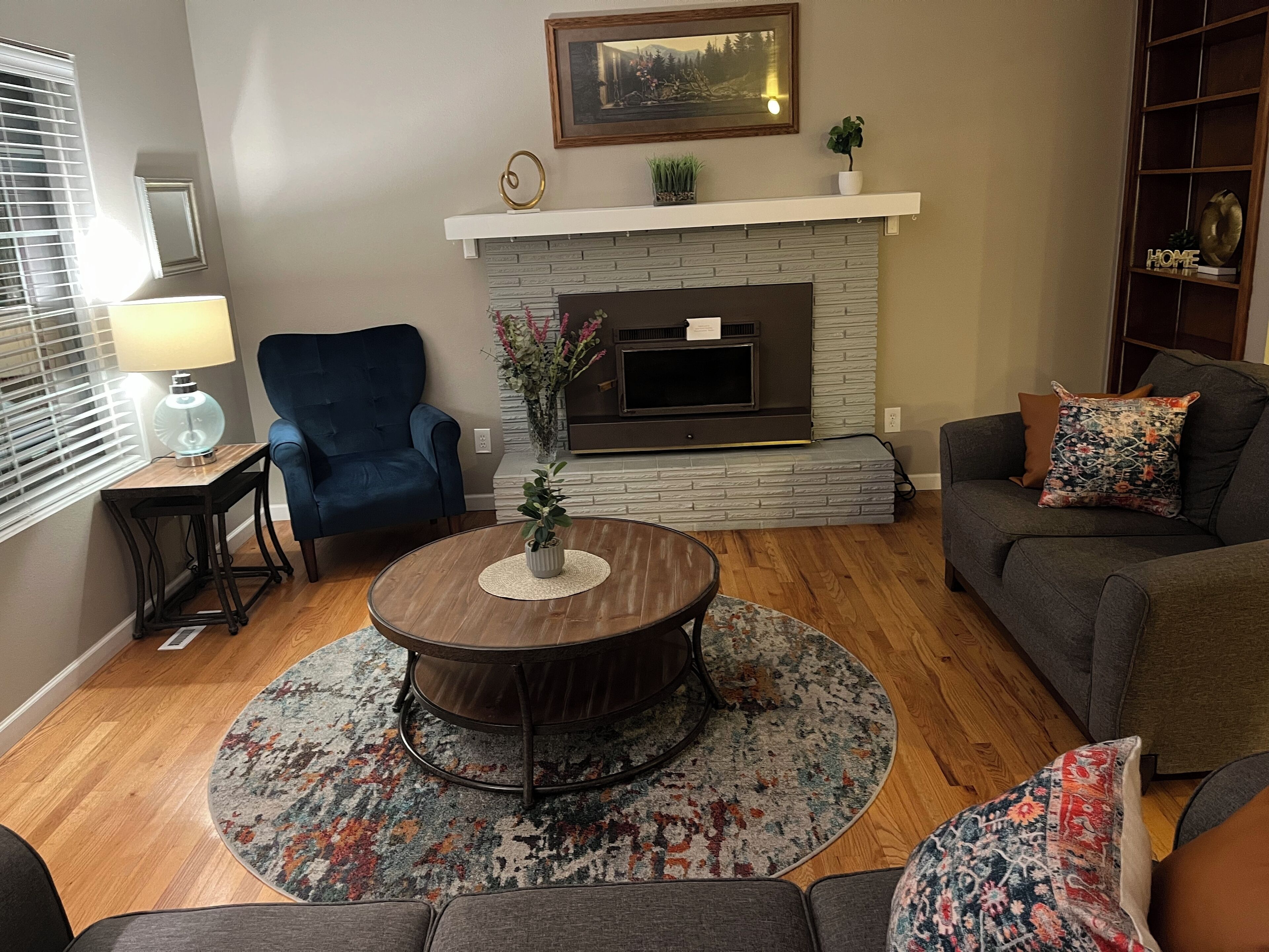 A living room with a fireplace, a blue armchair, a round coffee table, and a gray sofa.