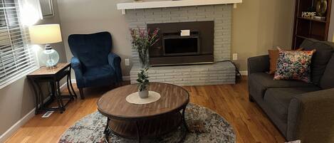 A living room with a fireplace, a blue armchair, a round coffee table, and a gray sofa.