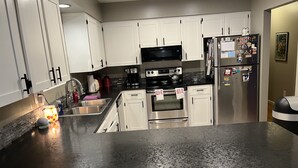 A modern kitchen with white cabinets, stainless steel appliances, and a granite countertop. - The Tangerine Door (Lewiston)