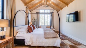Une chambre à coucher avec un lit à baldaquin, un téléviseur fixé au mur et un plafond en bois.