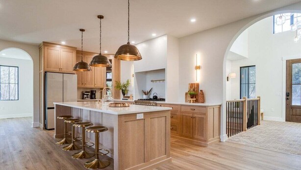Une cuisine spacieuse avec des meubles en bois, un îlot central doté de tabourets, un éclairage suspendu et une vue sur l’extérieur.