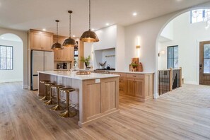 A spacious kitchen with wooden cabinets, a central island with stools, pendant lighting, and a view to the outdoors.