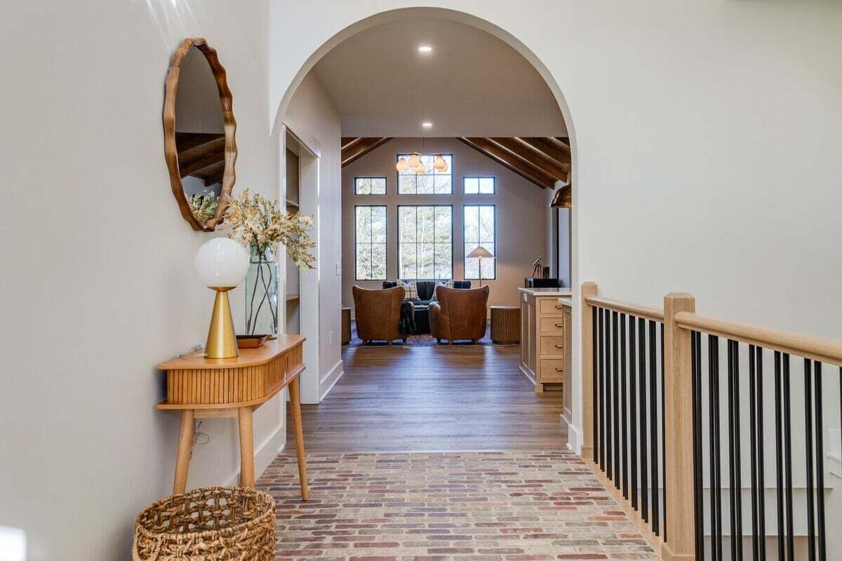 Un couloir avec un plancher en bois, un miroir, un vase de fleurs, une console en bois et un panier en osier.