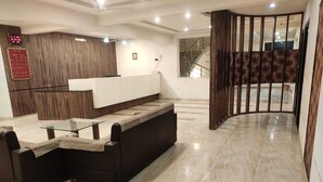 Un área de recepción con mostrador, un sofá, una mesa de centro de vidrio y una escalera que conduce a un piso superior.