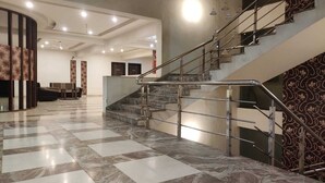 Un vestíbulo amplio con piso de mármol, un mostrador de recepción curvo y una escalera con barandillas de metal.