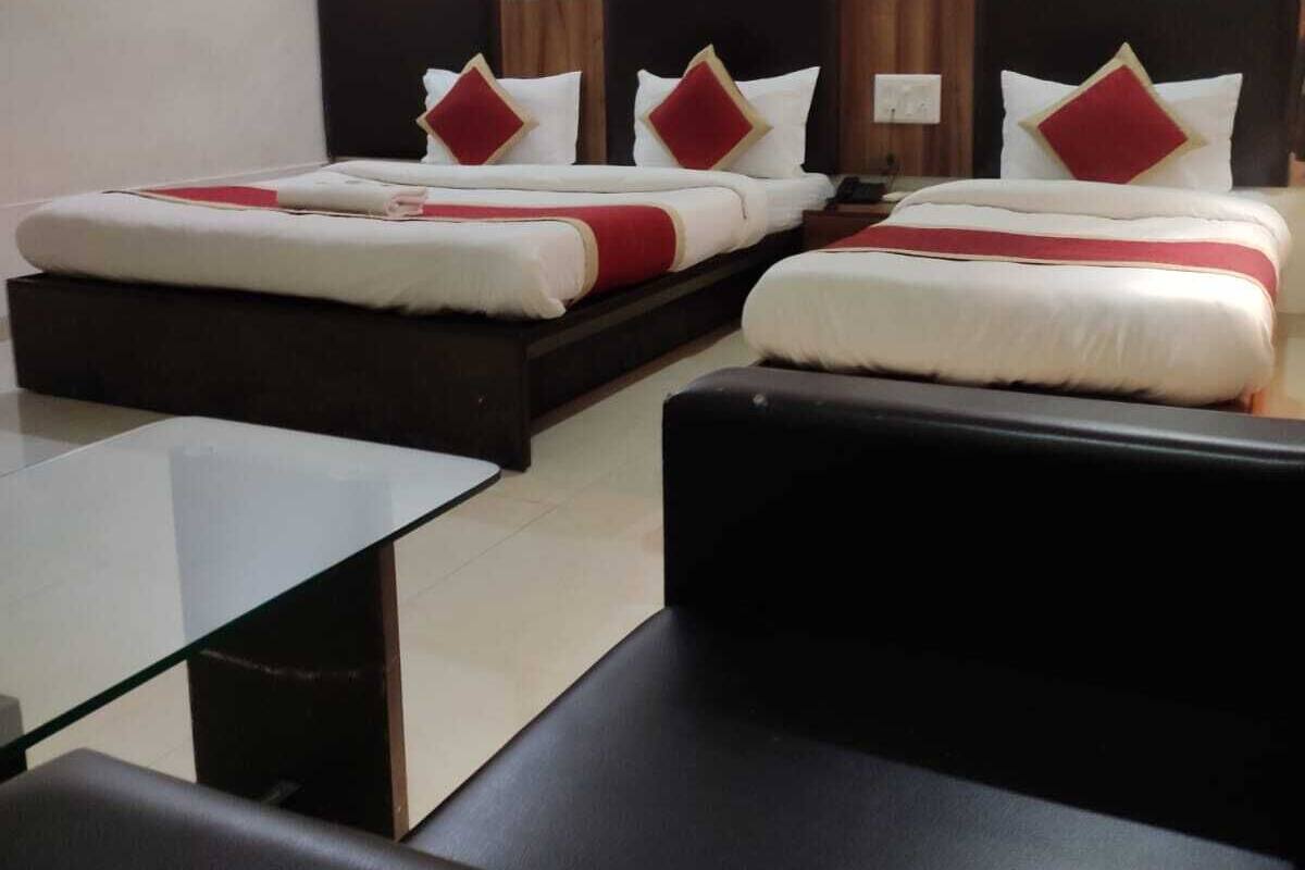 Habitación de hotel con dos camas, una mesa de vidrio y un sofá negro.