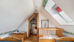 Una habitación con techo inclinado, una cuna de madera, un escritorio con una silla y una pequeña mesa con una silla.