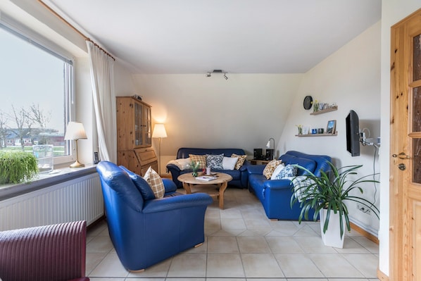 Un salon avec des canapés bleus, un meuble en bois, une lampe et une vue par la fenêtre.