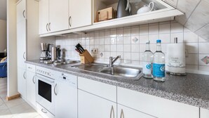 Una cocina con armarios blancos, encimera de granito, horno integrado, lavavajillas, fregadero y cafetera.