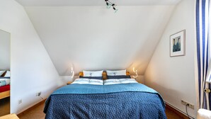 Ein Schlafzimmer mit Bett, Nachttisch, Sessel und Wandleuchte.