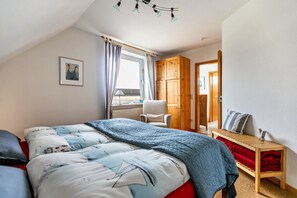 A bedroom with a bed, a chair, a wooden wardrobe, a window with curtains, and a picture on the wall.