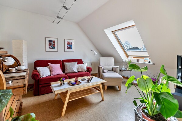 A cozy living room with a red sofa, a wooden coffee table, a white armchair, and a view through a skylight.