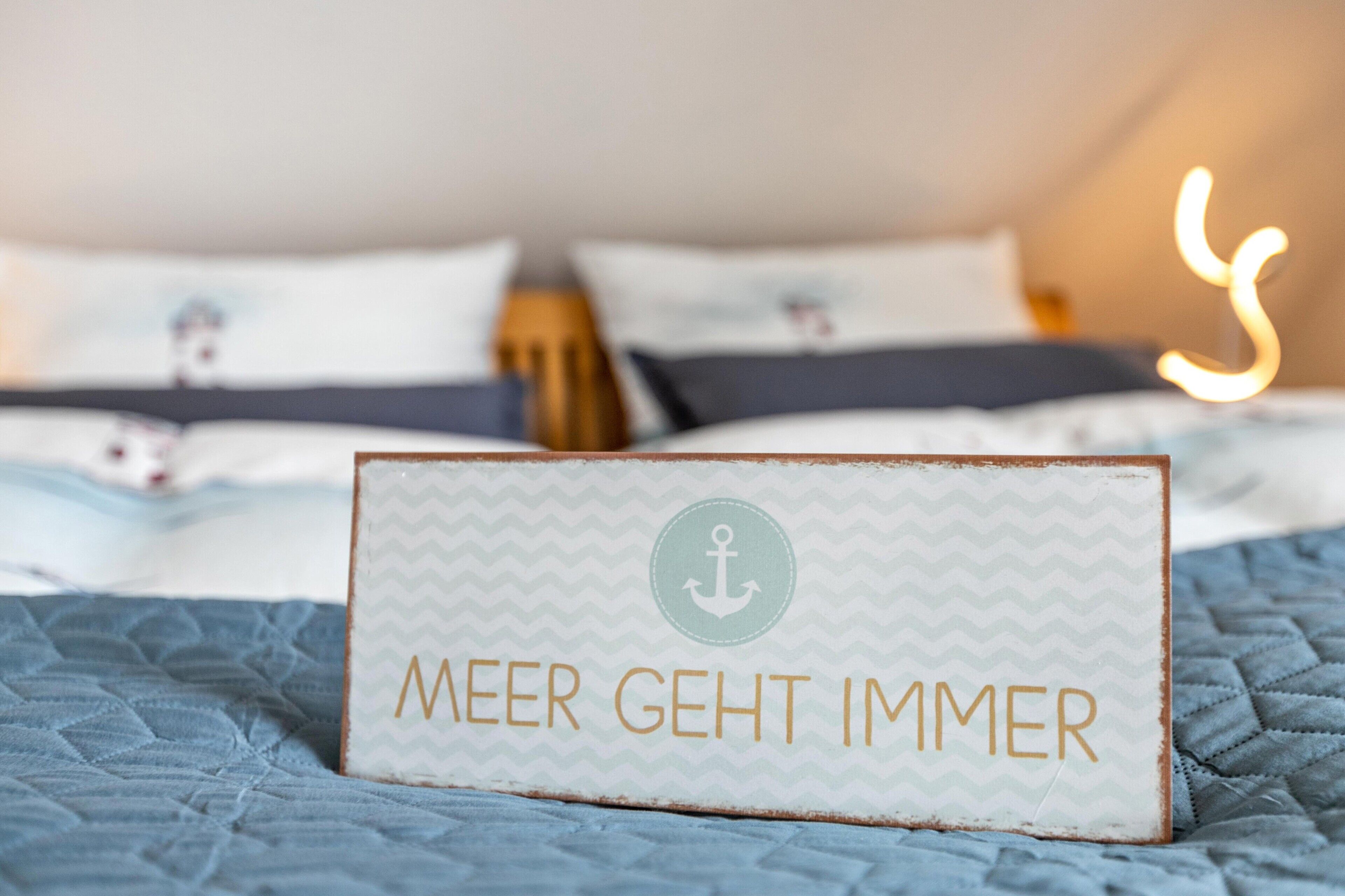 Un lit avec une pancarte sur laquelle on peut lire « MEER GEHT IMMER » et une lumière floue en arrière-plan.