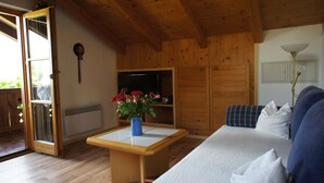 Un interior de madera con un sofá, una mesa con un jarrón de flores, un reloj y una puerta que da al exterior.