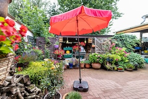 Un jardín con una sombrilla roja, plantas en macetas y una estructura de madera.