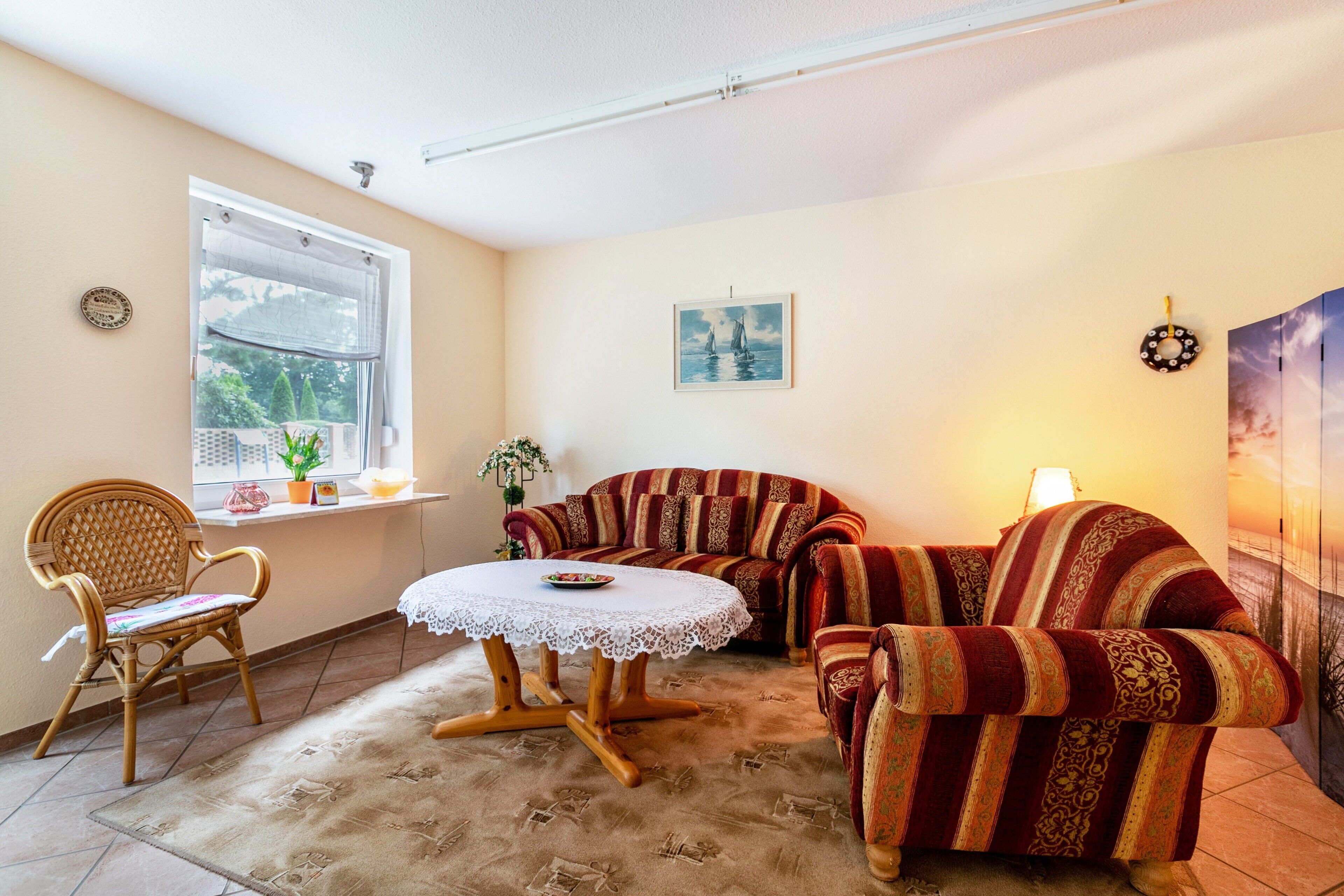 A cozy living room with a sofa, a chair, a small table, and a window with plants.