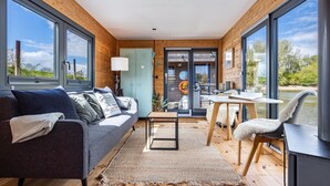 Ein modernes Interieur mit einer Couch, Tisch und Stühlen, großen Fenstern und Blick ins Freie.